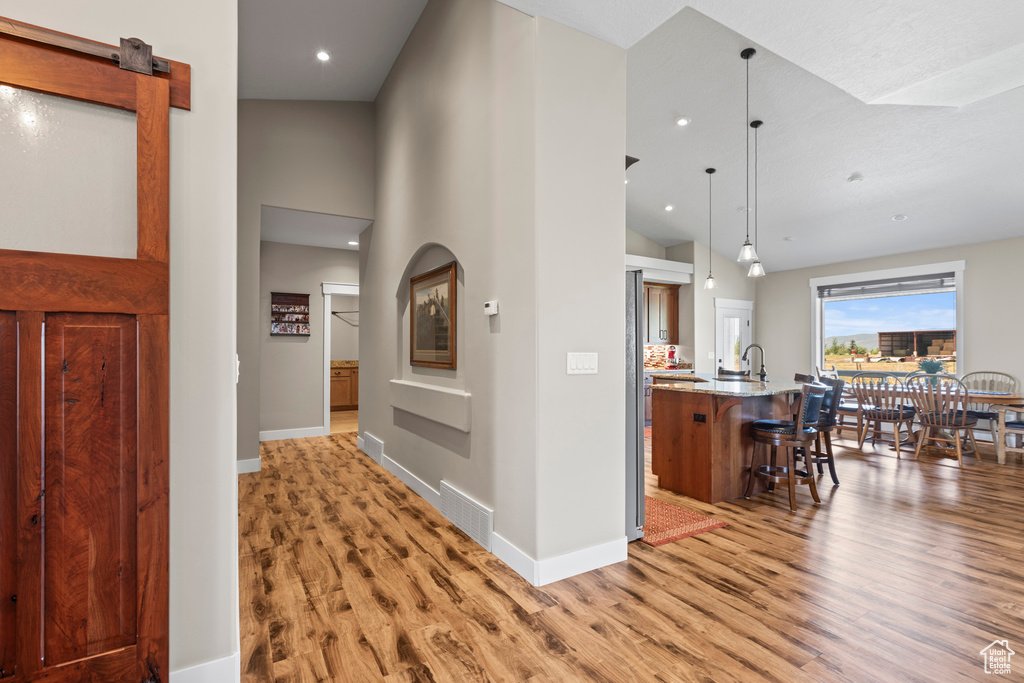 Corridor featuring high vaulted ceiling, sink, and light wood-type flooring