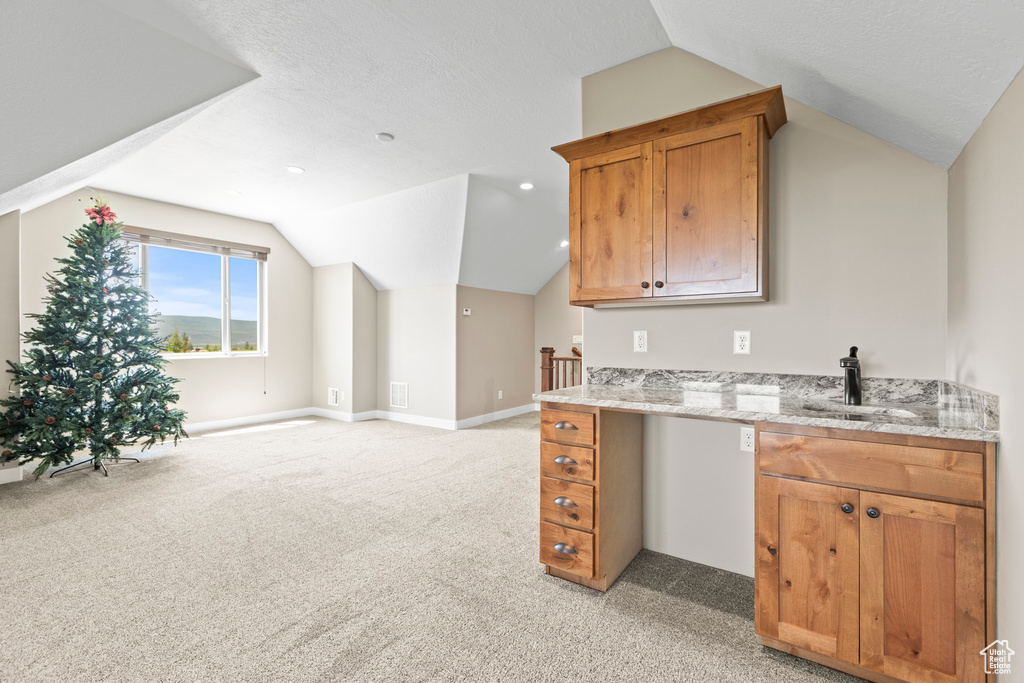 Kitchen featuring a textured ceiling, light stone counters, sink, vaulted ceiling, and light colored carpet