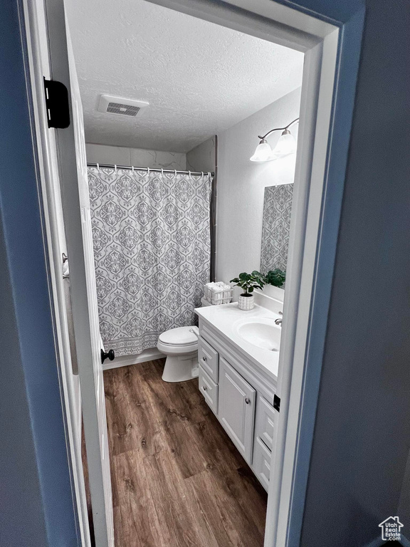 Bathroom with a textured ceiling, wood-type flooring, vanity, and toilet