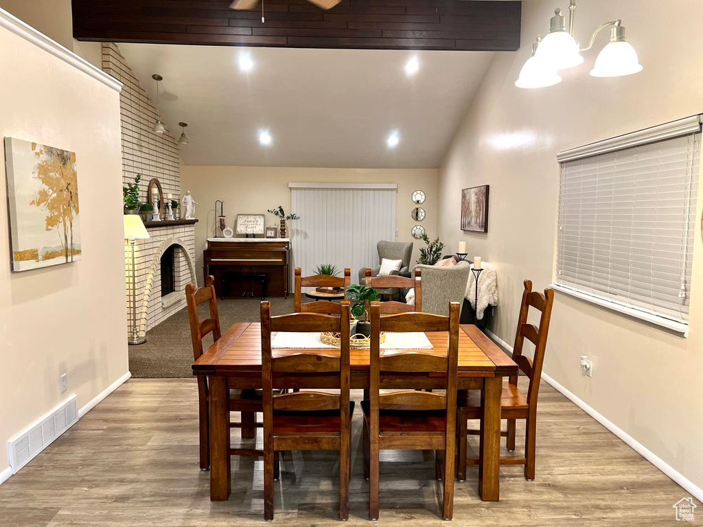 Dining area featuring beamed ceiling, high vaulted ceiling, hardwood / wood-style flooring, and a brick fireplace