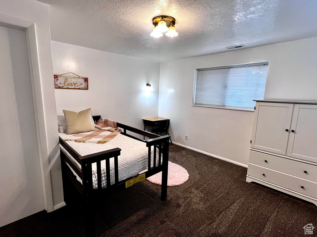 Bedroom with dark colored carpet and a textured ceiling