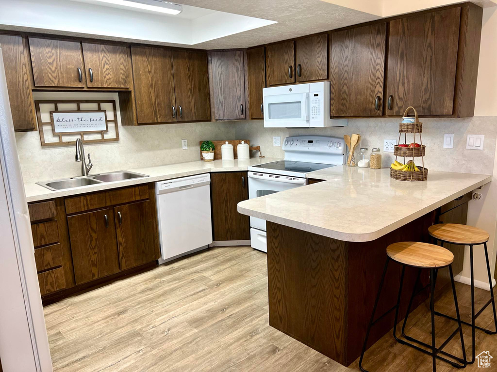 Kitchen featuring light hardwood / wood-style floors, kitchen peninsula, white appliances, sink, and a breakfast bar area