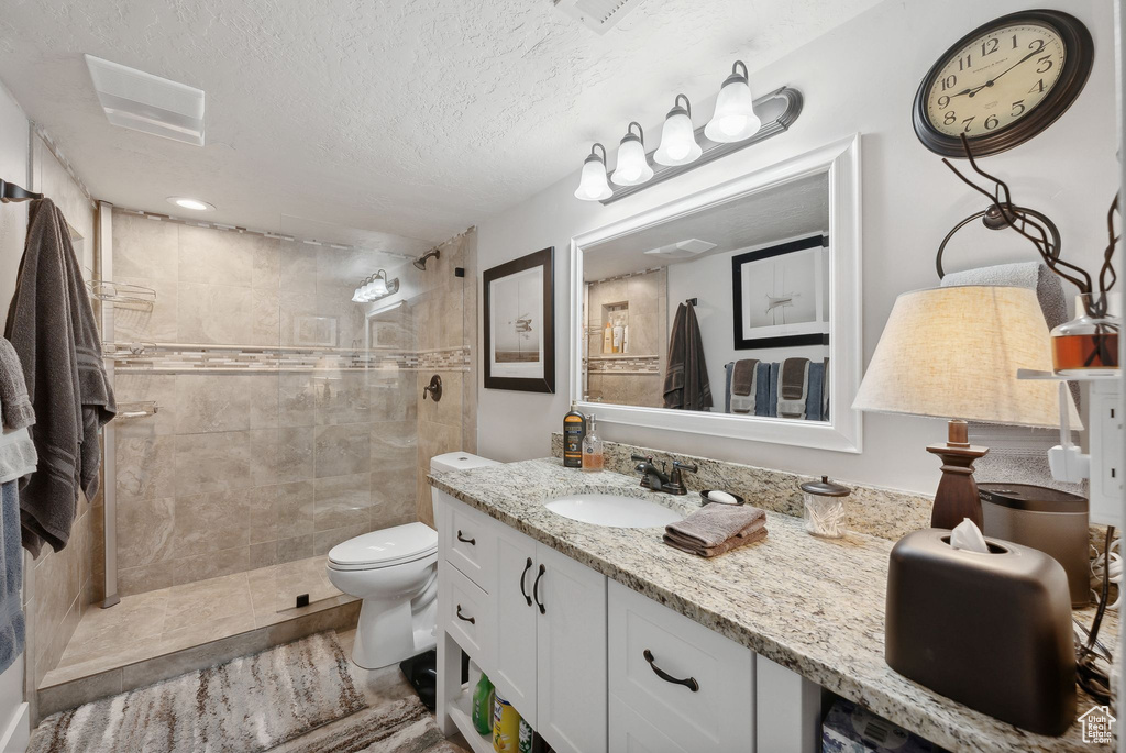 Bathroom featuring a tile shower, a textured ceiling, vanity, and toilet