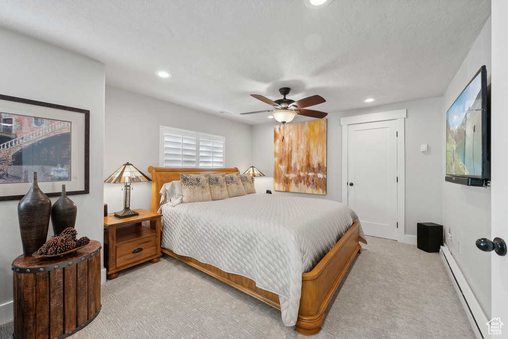 Bedroom with a textured ceiling, baseboard heating, ceiling fan, and light colored carpet