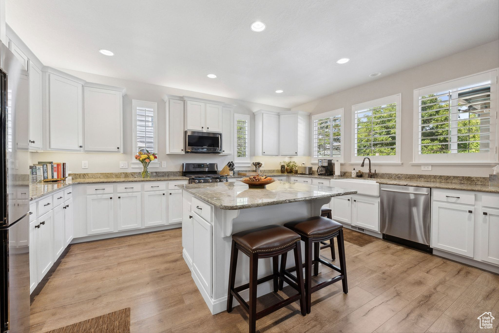 Kitchen featuring a kitchen breakfast bar, a kitchen island, light hardwood / wood-style flooring, appliances with stainless steel finishes, and white cabinets