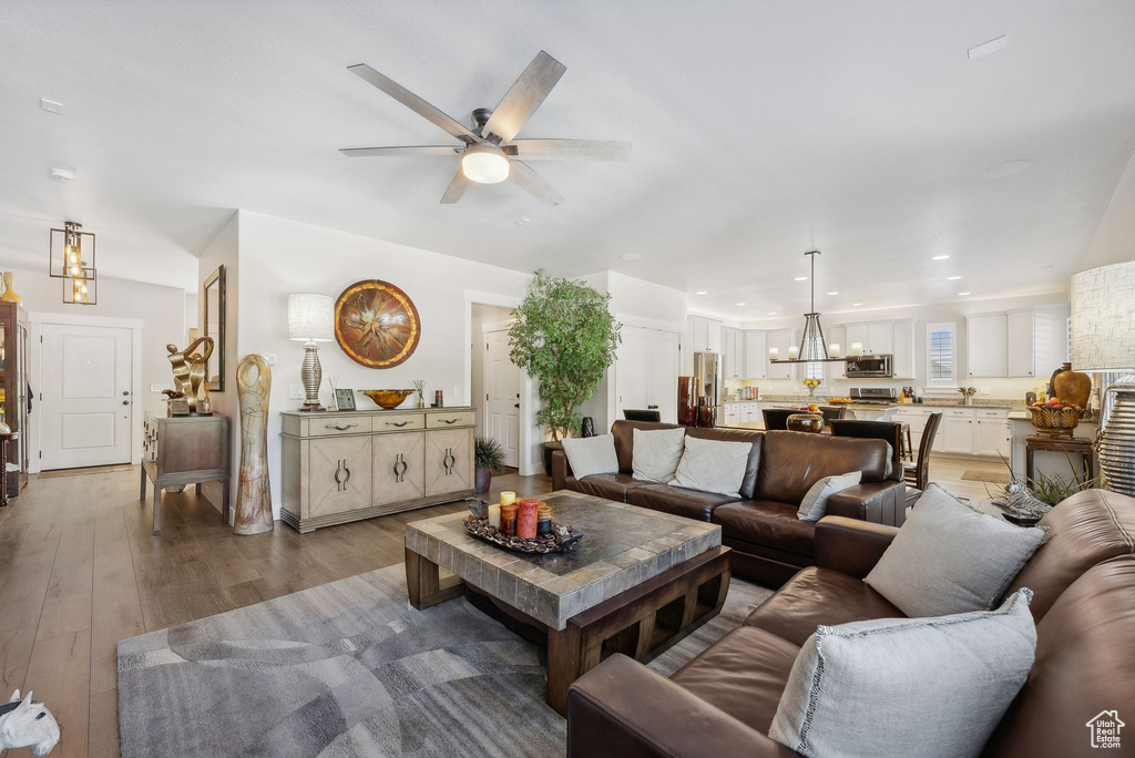 Living room featuring ceiling fan with notable chandelier and wood-type flooring