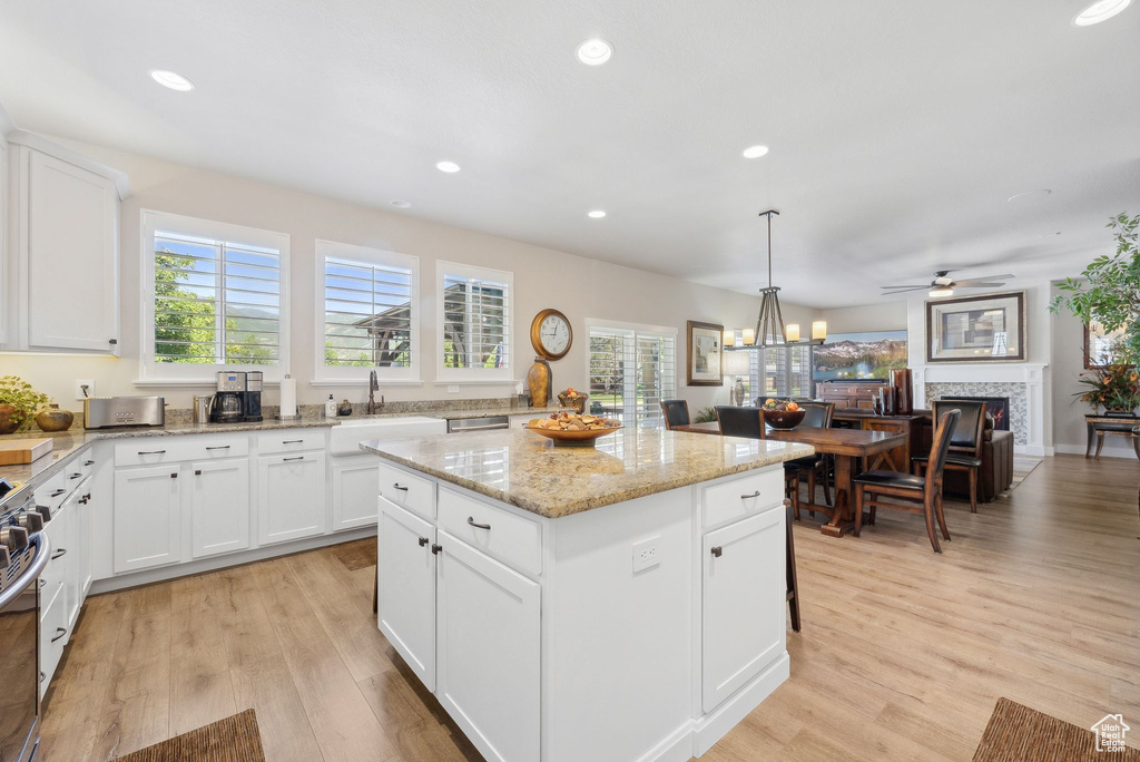 Kitchen with a center island, white cabinets, light wood-type flooring, and light stone counters