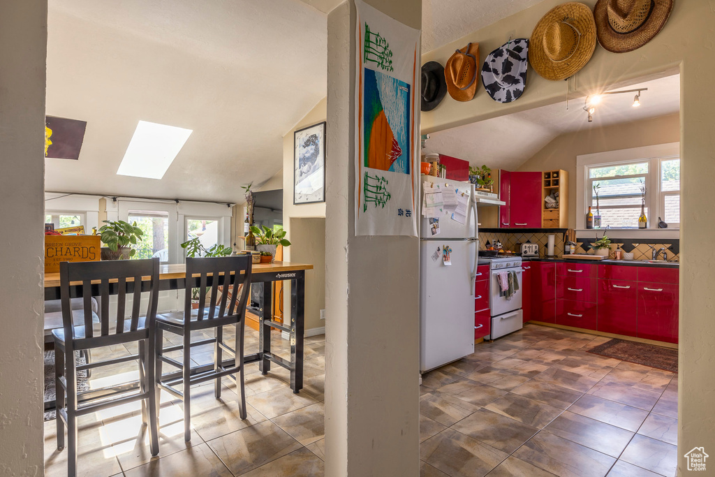 Kitchen with white appliances, a healthy amount of sunlight, vaulted ceiling with skylight, and tasteful backsplash