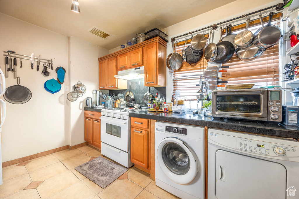 Kitchen featuring white gas range oven, washer and clothes dryer, backsplash, and light tile floors