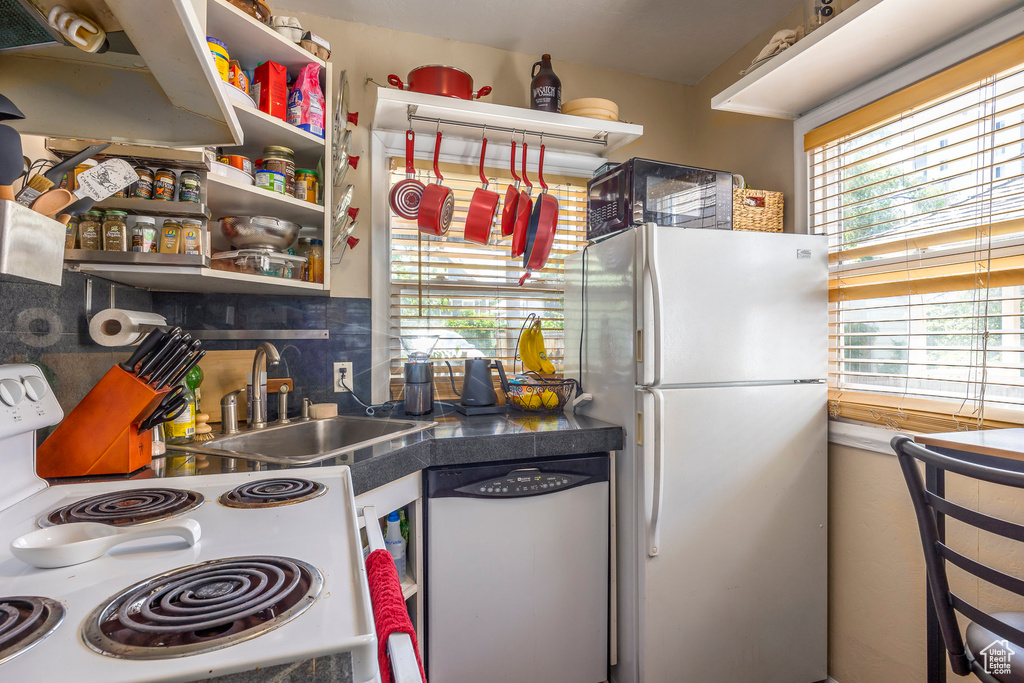 Kitchen featuring dishwasher, white refrigerator, stove, backsplash, and sink