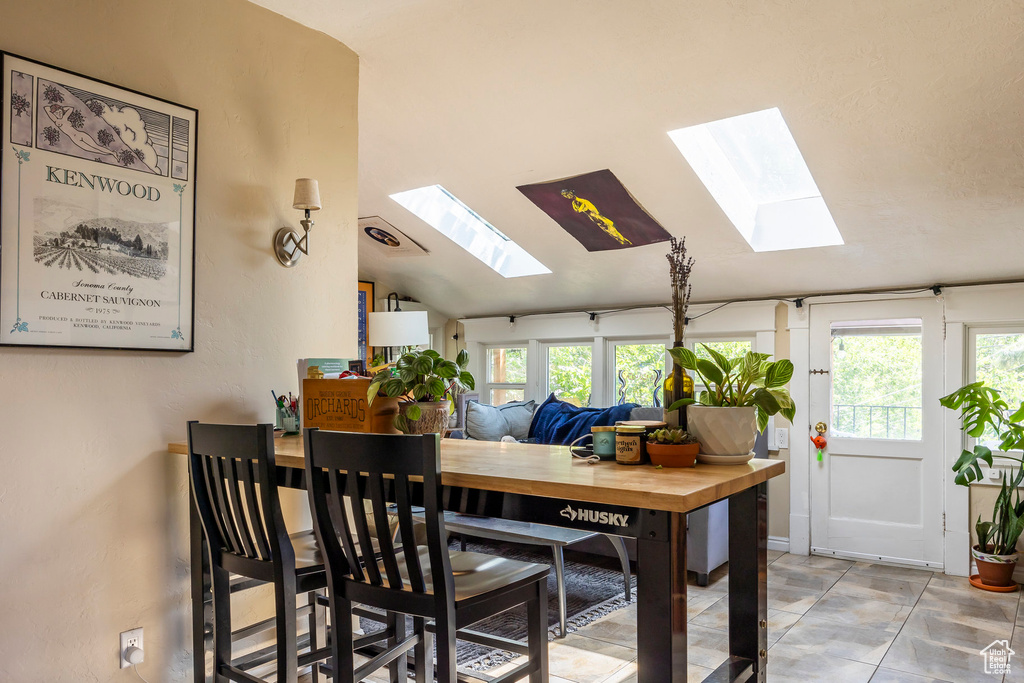 Dining room with tile flooring and lofted ceiling with skylight