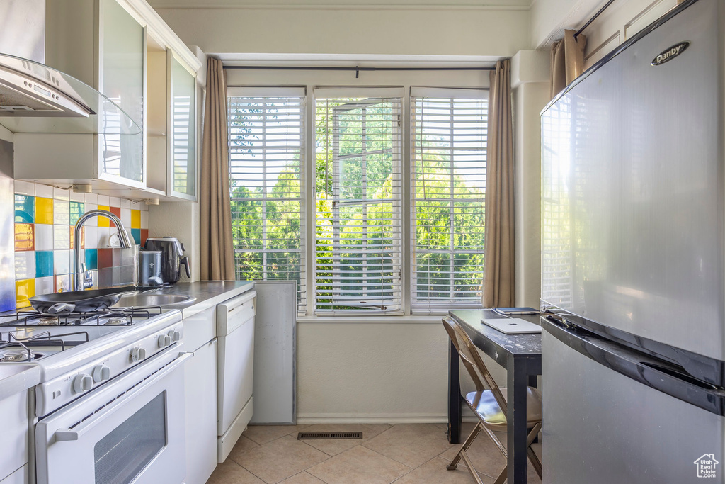 Kitchen with white appliances, light tile flooring, plenty of natural light, and wall chimney exhaust hood