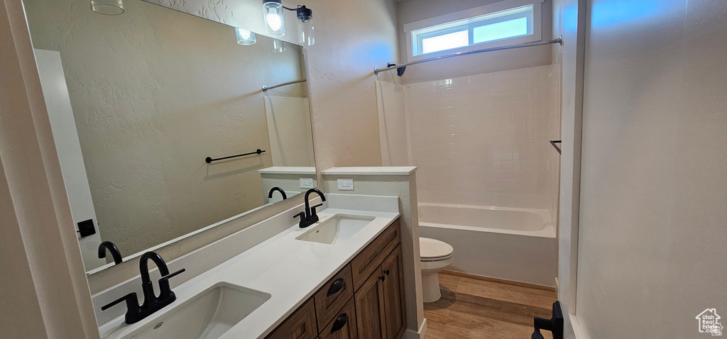 Full bathroom with double vanity, toilet, hardwood / wood-style flooring, and shower / washtub combination