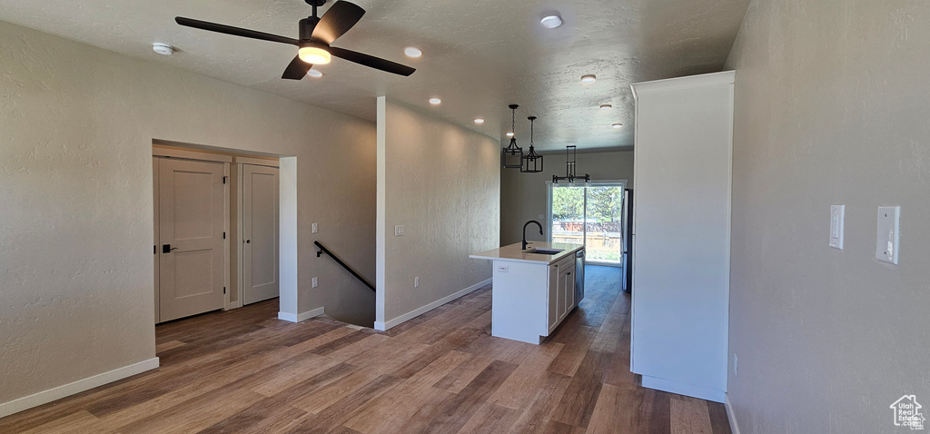 Kitchen with hanging light fixtures, a center island with sink, ceiling fan, and light hardwood / wood-style floors