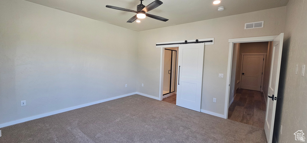 Unfurnished bedroom featuring a barn door, carpet flooring, and ceiling fan