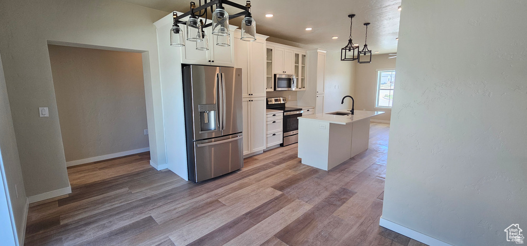 Kitchen with a center island with sink, hanging light fixtures, hardwood / wood-style flooring, white cabinets, and appliances with stainless steel finishes