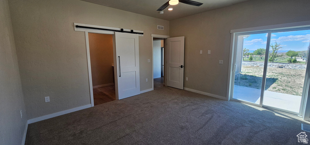 Unfurnished bedroom featuring a barn door, access to outside, carpet, and ceiling fan