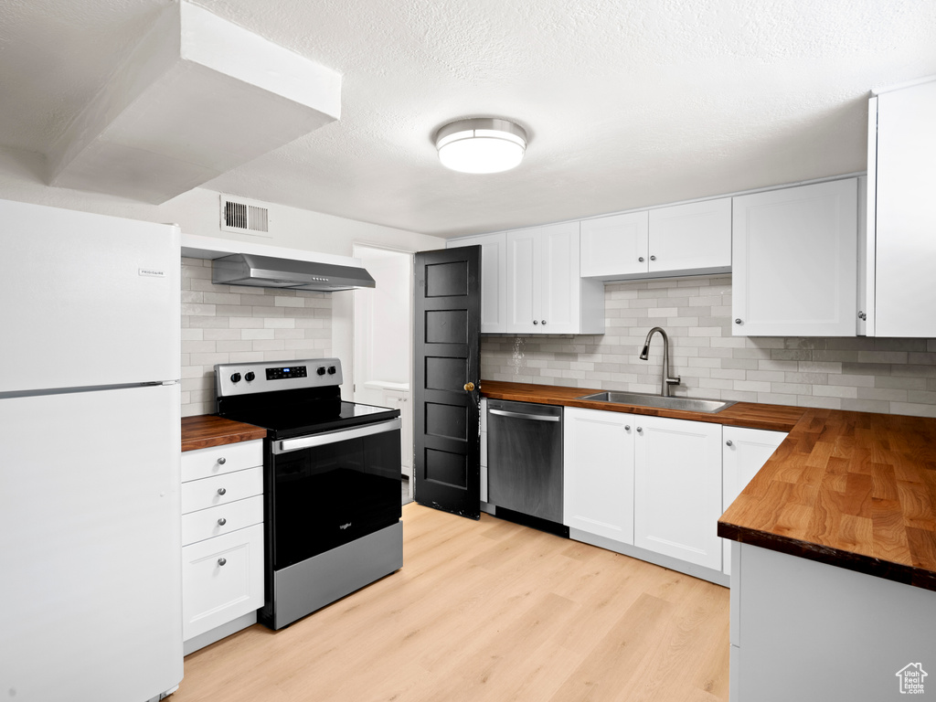 Kitchen with light hardwood / wood-style floors, tasteful backsplash, stainless steel appliances, butcher block counters, and white cabinetry