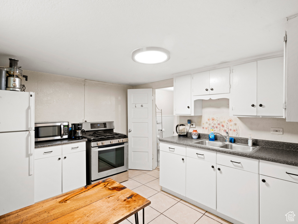 Kitchen with appliances with stainless steel finishes, white cabinetry, sink, and light tile flooring