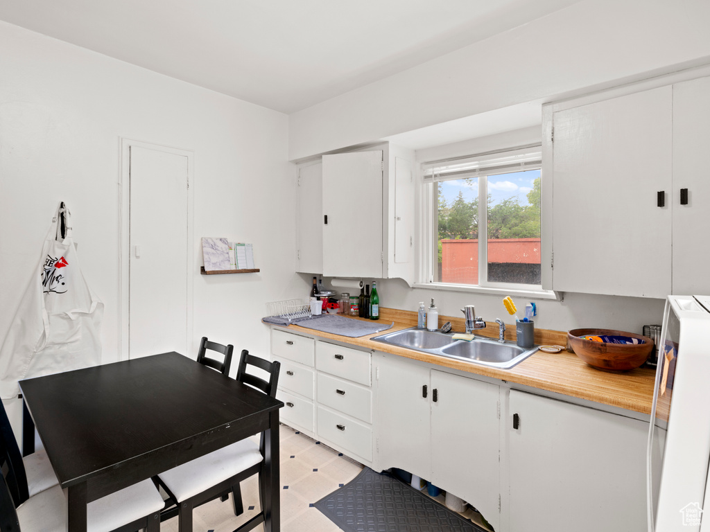 Kitchen with washer / dryer, white cabinets, sink, and light tile floors