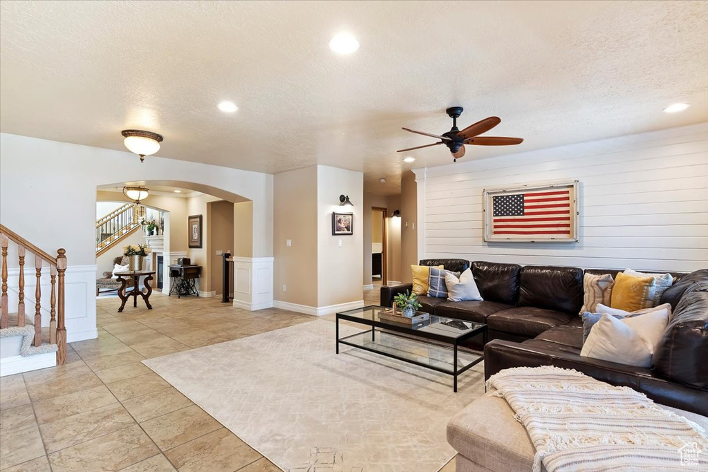 Living room with a textured ceiling, light tile flooring, and ceiling fan