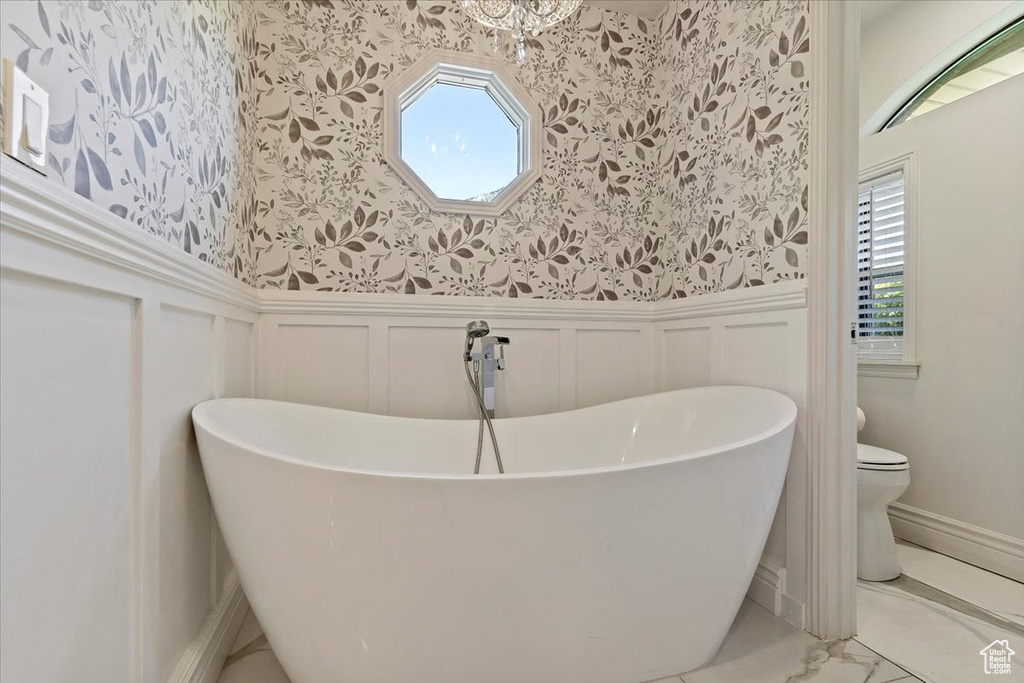 Bathroom featuring a healthy amount of sunlight, a tub, toilet, and tile floors