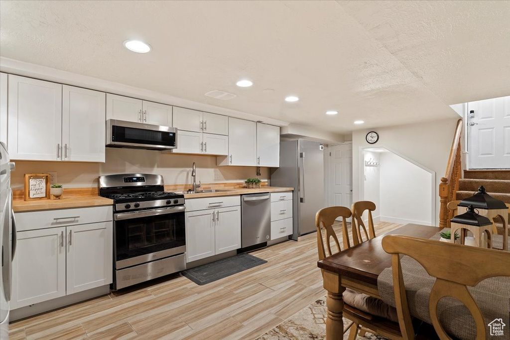 Kitchen with light hardwood / wood-style flooring, white cabinets, and appliances with stainless steel finishes