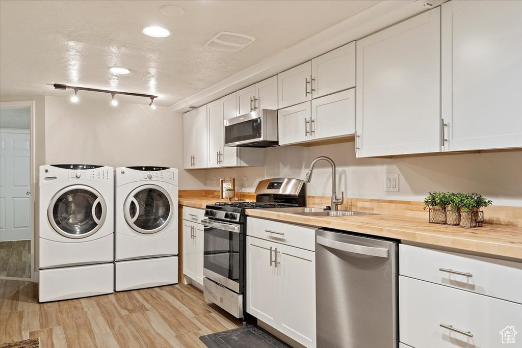 Kitchen featuring washer and dryer, butcher block counters, light hardwood / wood-style flooring, appliances with stainless steel finishes, and white cabinets