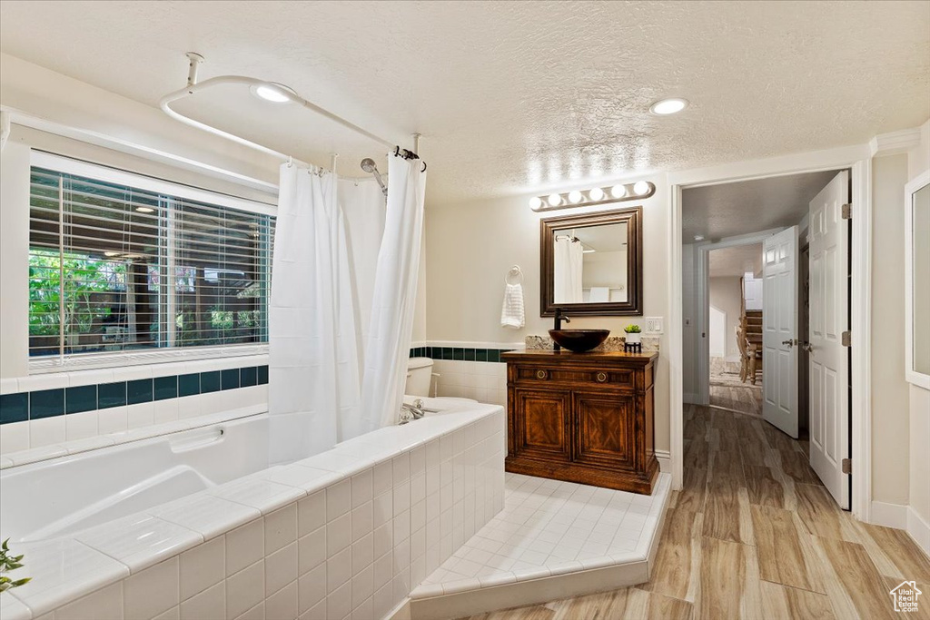 Bathroom featuring wood-type flooring, tiled bath, a textured ceiling, and large vanity