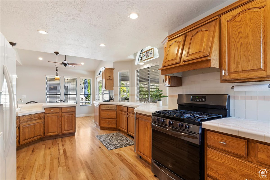 Kitchen with hanging light fixtures, light hardwood / wood-style flooring, tile countertops, backsplash, and gas range