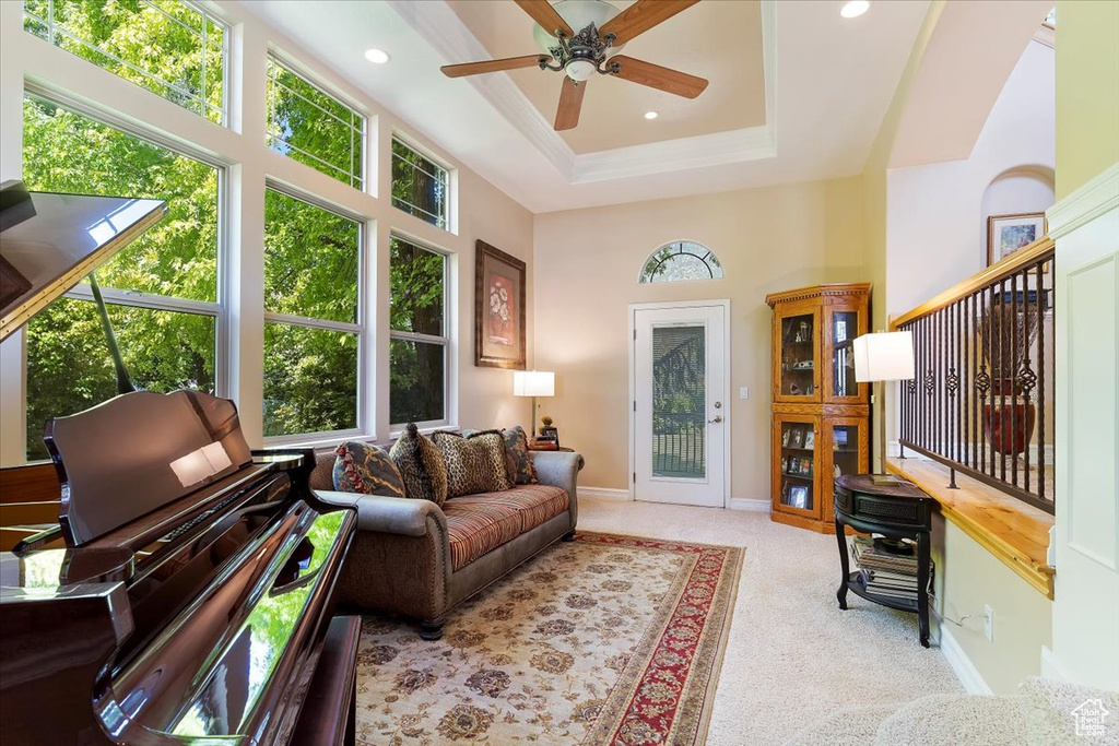 Carpeted living room featuring a high ceiling, ceiling fan, and a tray ceiling