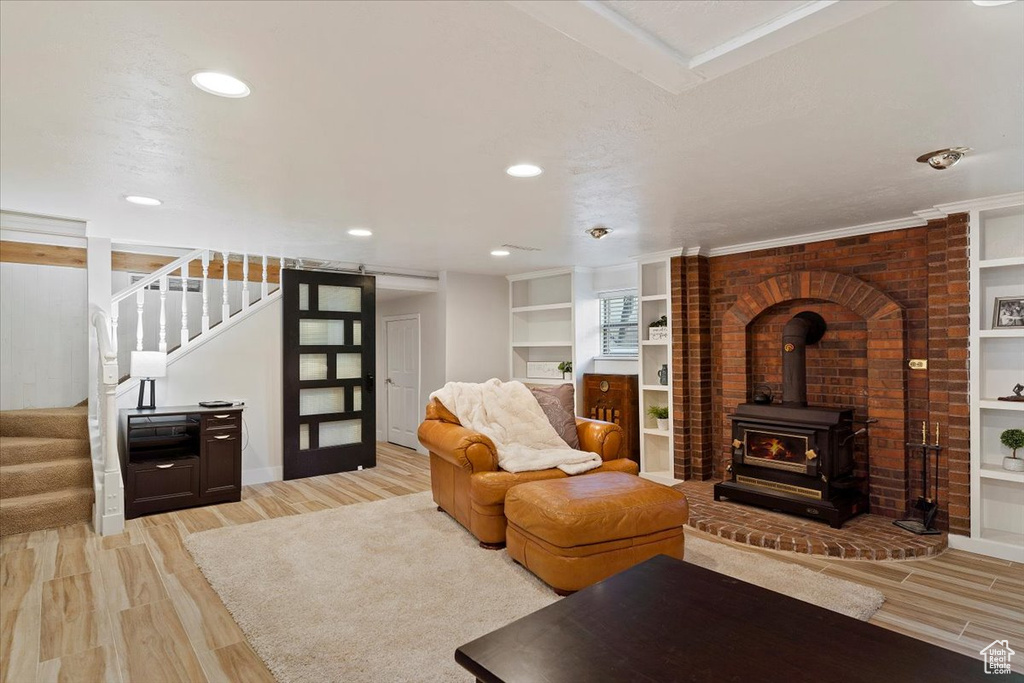 Living room featuring built in shelves, light wood-type flooring, a wood stove, and brick wall