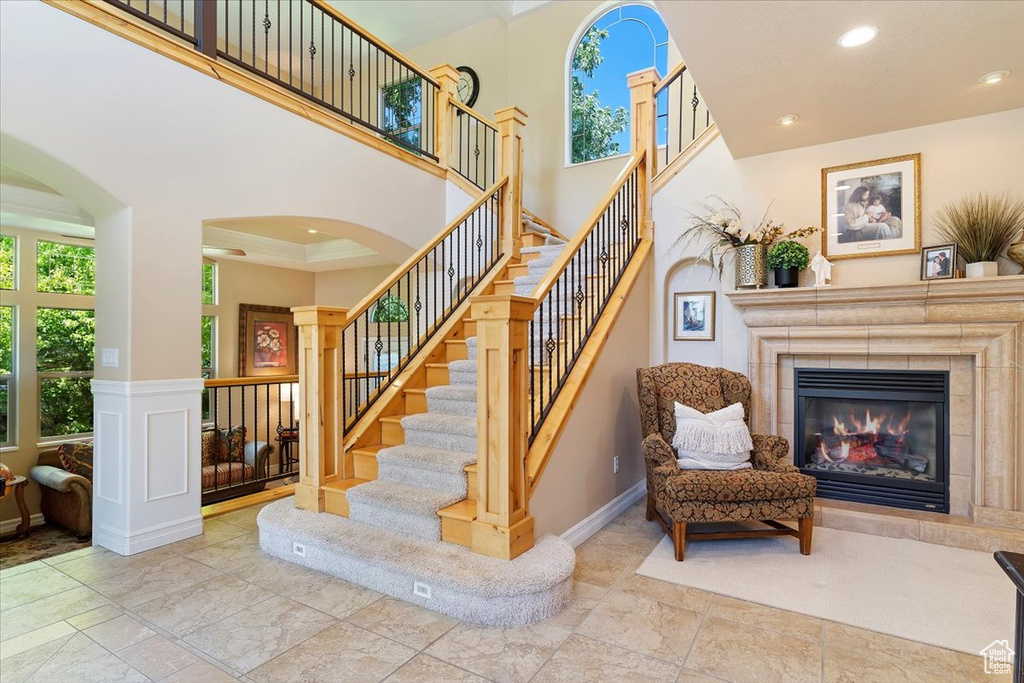 Staircase with tile flooring, a tiled fireplace, crown molding, ornate columns, and a towering ceiling