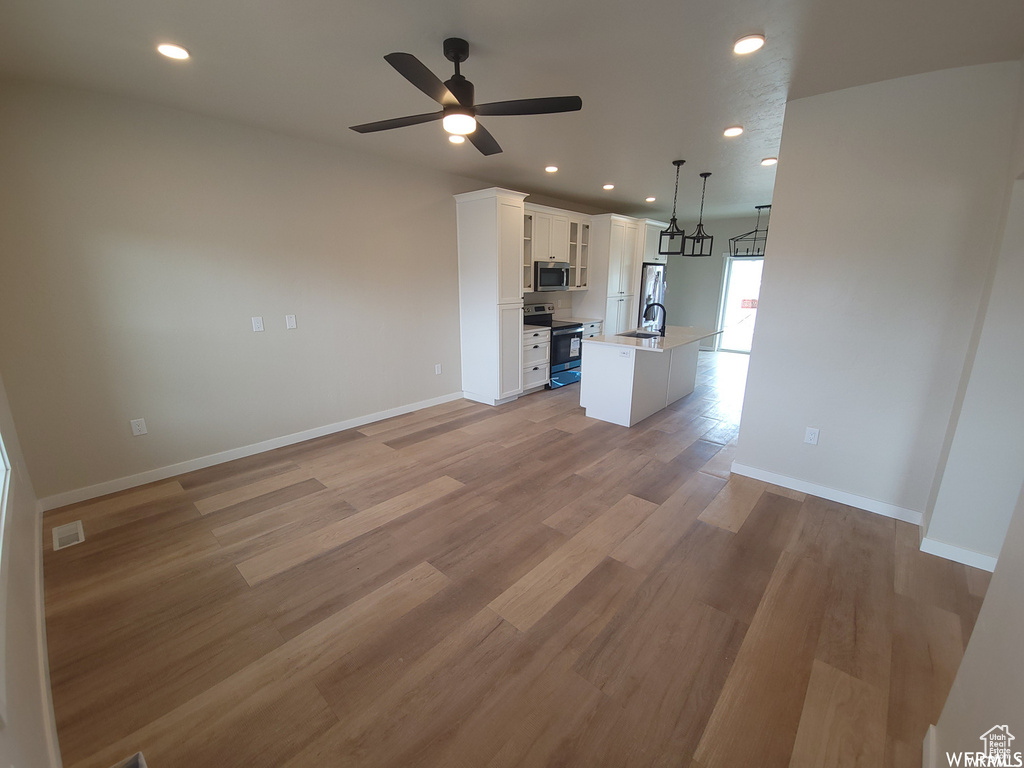 Unfurnished living room featuring sink, ceiling fan, and light wood-type flooring