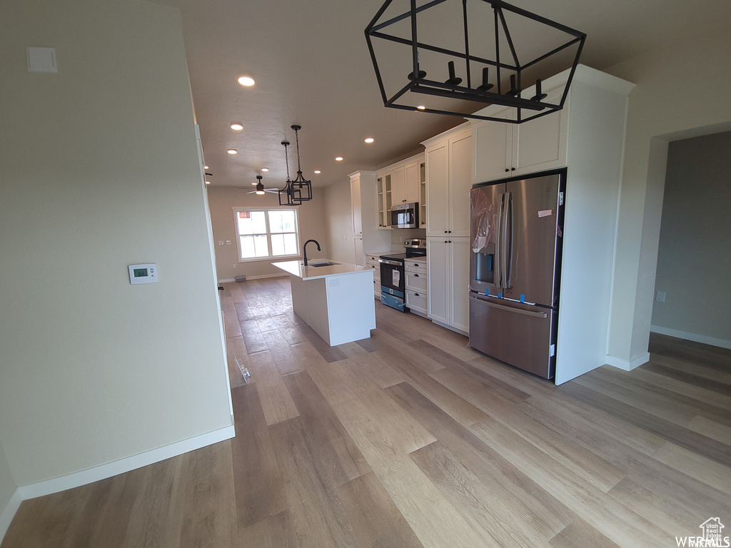 Kitchen with an island with sink, light wood-type flooring, pendant lighting, and appliances with stainless steel finishes