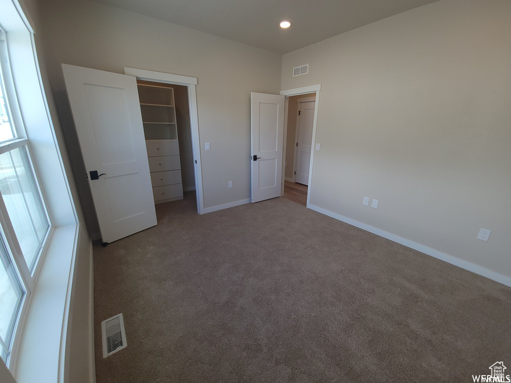 Unfurnished bedroom with a walk in closet, a closet, and carpet