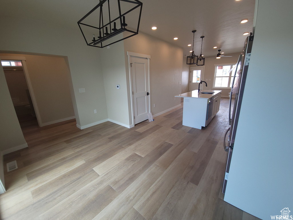 Kitchen featuring an island with sink, decorative light fixtures, and light wood-type flooring