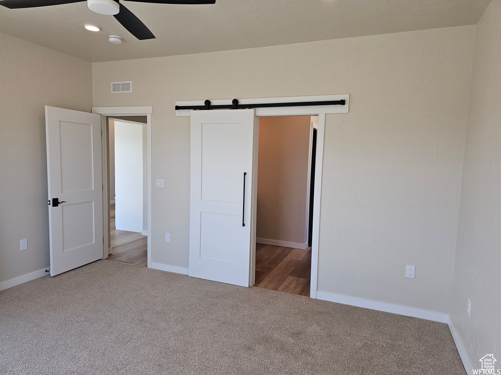 Unfurnished bedroom with a barn door, ceiling fan, and carpet flooring