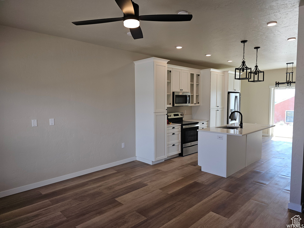 Kitchen with hanging light fixtures, appliances with stainless steel finishes, dark hardwood / wood-style flooring, and a kitchen island with sink