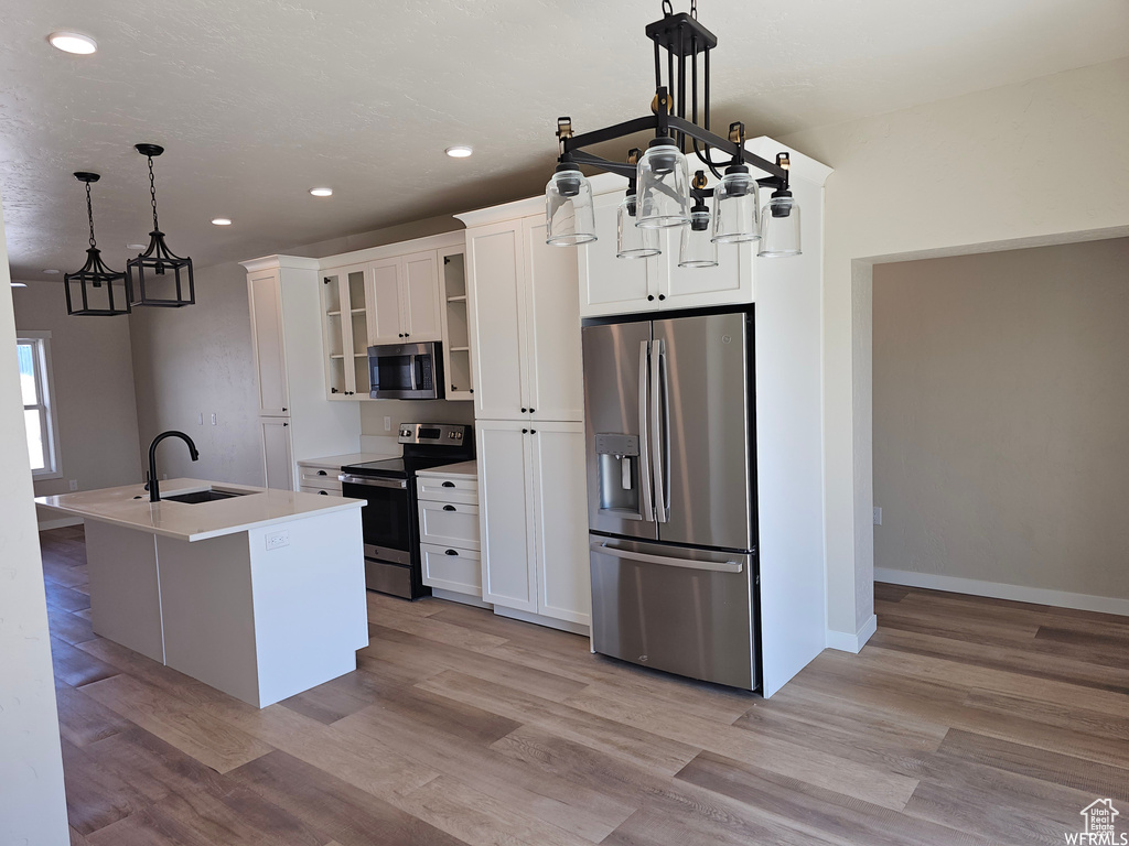 Kitchen with light hardwood / wood-style floors, hanging light fixtures, stainless steel appliances, white cabinets, and sink