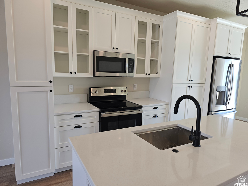 Kitchen with appliances with stainless steel finishes, sink, white cabinets, and wood-type flooring