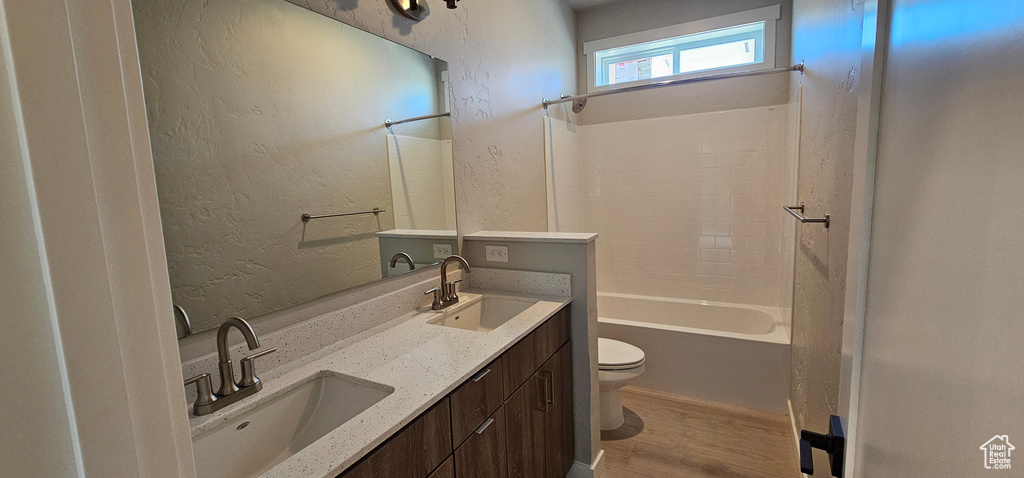 Full bathroom with hardwood / wood-style flooring,  shower combination, double sink vanity, and toilet