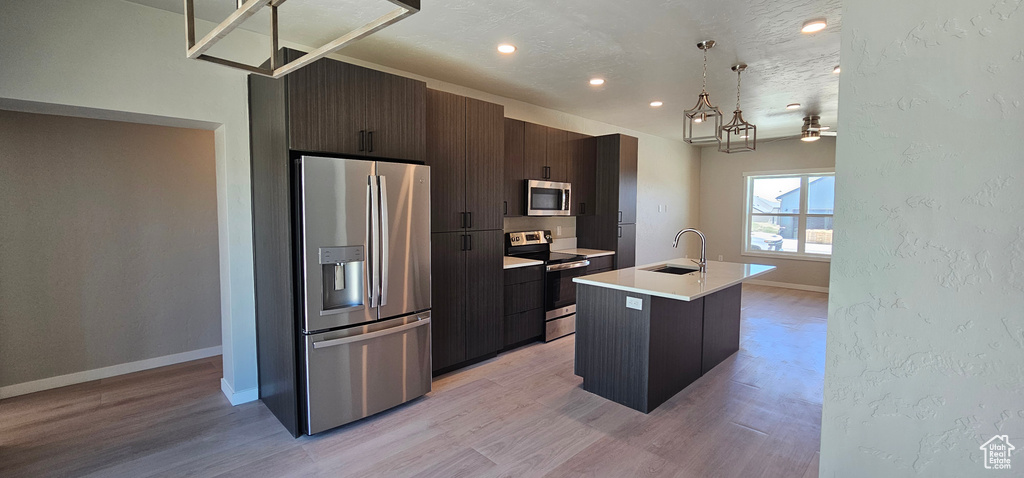 Kitchen featuring ceiling fan, sink, appliances with stainless steel finishes, light hardwood / wood-style flooring, and a kitchen island with sink