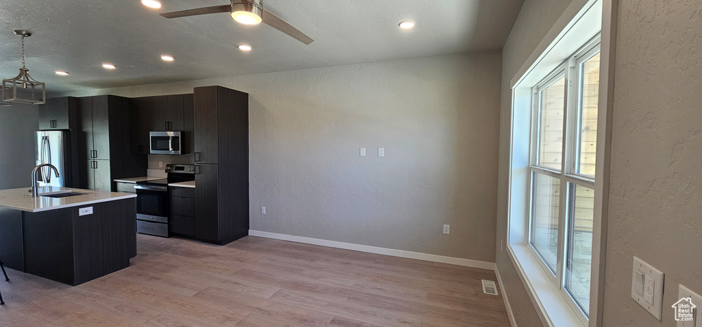 Kitchen featuring ceiling fan, hanging light fixtures, light wood-type flooring, sink, and appliances with stainless steel finishes