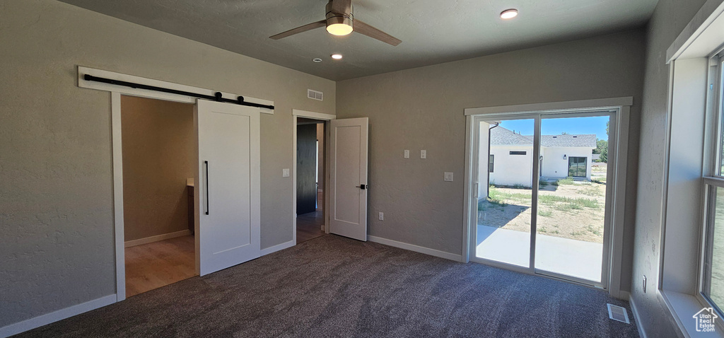 Unfurnished bedroom featuring access to outside, a barn door, carpet floors, and ceiling fan