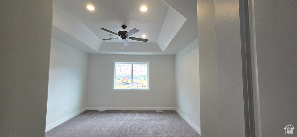 Carpeted spare room featuring ceiling fan and a tray ceiling