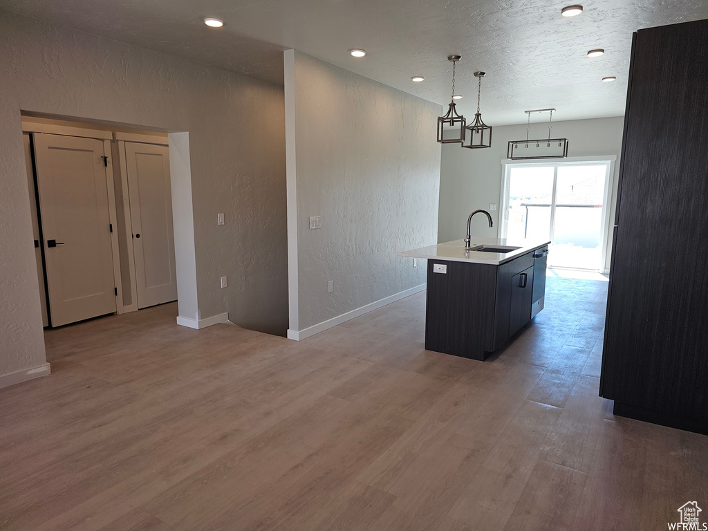 Kitchen with a center island with sink, decorative light fixtures, wood-type flooring, sink, and a chandelier