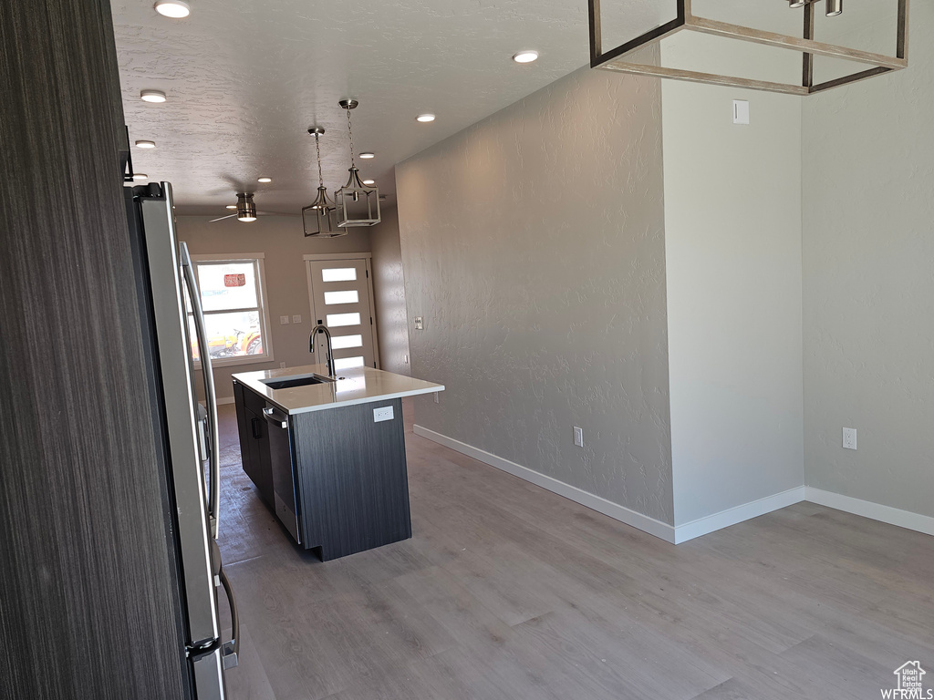 Kitchen featuring stainless steel appliances, hanging light fixtures, a center island with sink, hardwood / wood-style floors, and sink