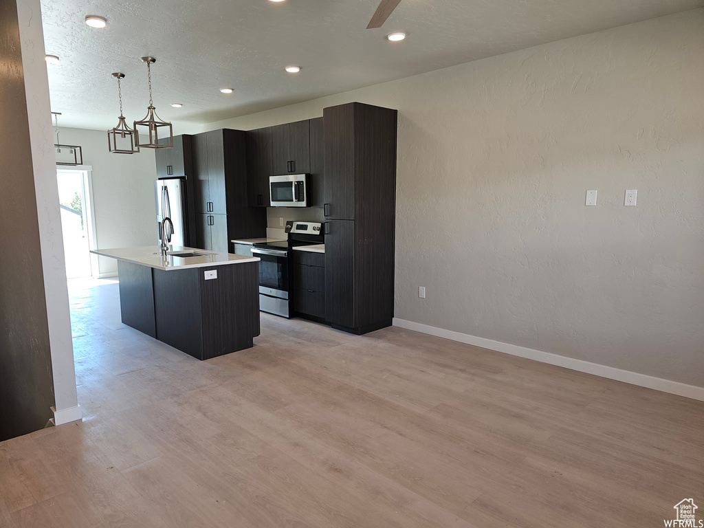 Kitchen featuring an island with sink, light hardwood / wood-style floors, decorative light fixtures, and appliances with stainless steel finishes