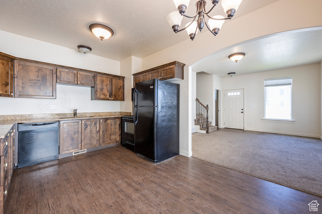 Kitchen featuring black appliances, dark wood-type flooring, light stone counters, and an inviting chandelier